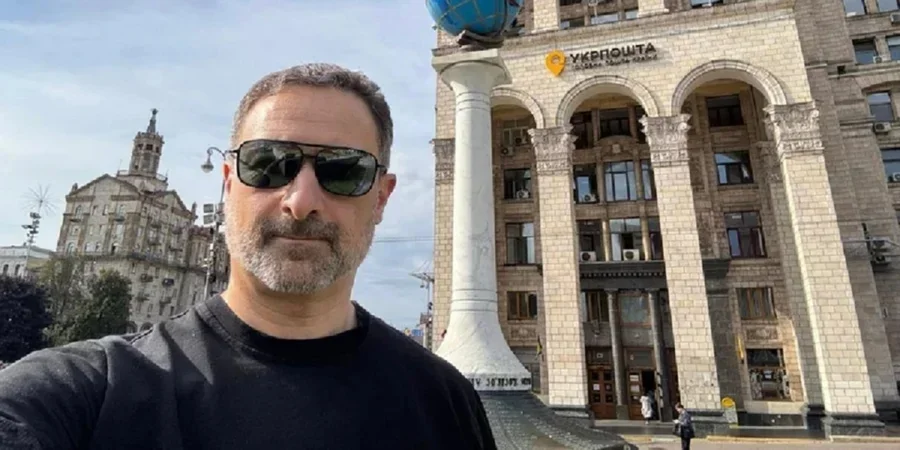 Чоловік у сонцезахисних окулярах робить селфі біля будівлі Укрпошти з глобусом